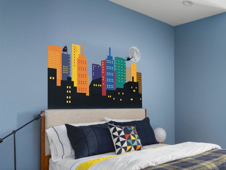 May include: A blue bedroom with a bed and a cityscape wall decal. The decal features a black silhouette of a city with colourful buildings and a helicopter flying over a full moon.