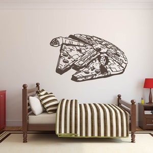 May include: A brown and white striped bedspread on a wooden bed frame with a brown and white striped pillow. A brown silhouette of the Millennium Falcon spaceship is on the wall behind the bed.