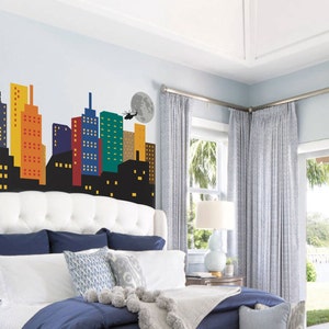 May include: A white headboard with a tufted design features a colourful cityscape wall decal. The decal includes a helicopter, a moon, and a figure standing on a building.