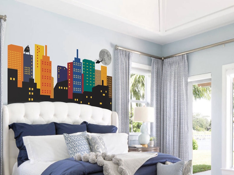 May include: A white headboard with a tufted design features a colourful cityscape wall decal. The decal includes a helicopter, a moon, and a figure standing on a building.