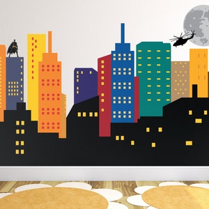 May include: A colourful cityscape wall decal featuring a black silhouette of a superhero standing on a building, a helicopter flying above, and a grey moon in the background.