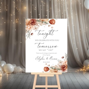 May include: A white wedding sign with floral accents in shades of brown and peach. The sign reads "Tonight, We Celebrate With You, Tomorrow We Say 'I Do'" with the names Skylar & Brian and the date 09.20.2025.