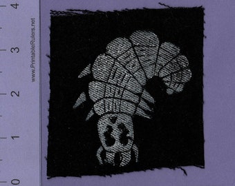 May include: A black fabric patch with a white embroidered image of a caterpillar. The caterpillar is facing left and has a segmented body.