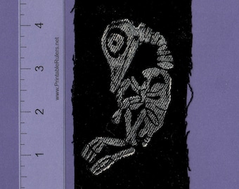 May include: A black fabric patch with a silver embroidered skeleton of a bird. The patch is approximately 2 inches wide and 3 inches tall.