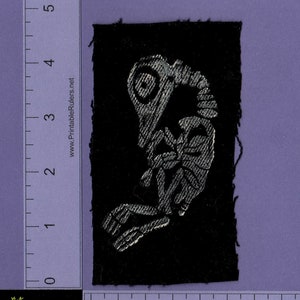 May include: A black fabric patch with a silver embroidered skeleton of a bird. The patch is approximately 2 inches wide and 3 inches tall.