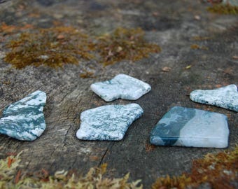 May include: Five irregularly shaped green and white agate stones on a rough, gray, wooden surface.