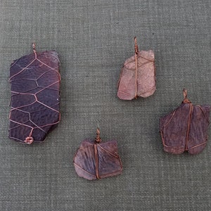 May include: Four handmade copper wire wrapped pendants with different shaped and colored stones. The stones are a dark purple, a light brown, and two dark brown stones.