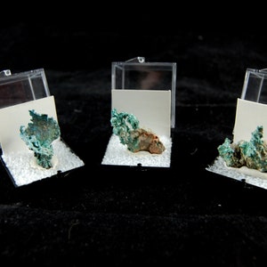 May include: Three small, clear plastic display boxes each containing a green and brown mineral specimen.