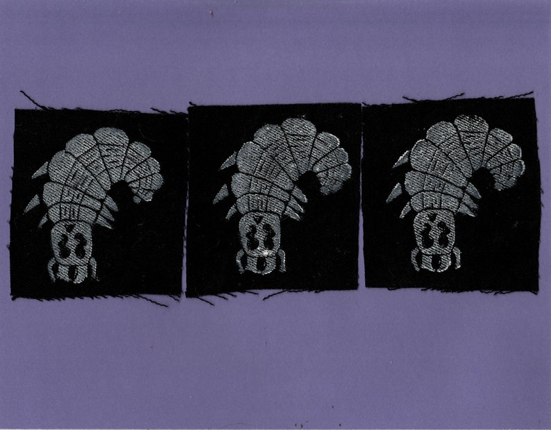 May include: Three black fabric patches with a silver embroidered design of a stylized insect. The insect is facing left and has a segmented body and legs.