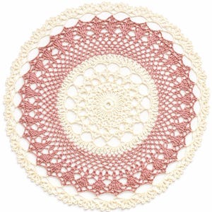 Puede incluir: Un tapete redondo de ganchillo en crema y rosa. El diseño presenta un círculo central crema, una banda rosa y un borde festoneado crema. El intrincado trabajo de ganchillo crea una apariencia delicada y de encaje. Diámetro aproximado de 25 cm.