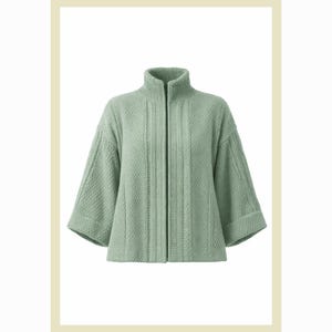 Puede incluir: Chaqueta verde claro texturizada con cuello alto y cremallera negra completa. La chaqueta tiene mangas tres cuartos y un sutil patrón tejido. La prenda se muestra sobre un fondo blanco con un marco beige claro.