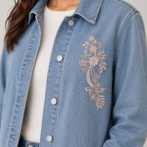 Könnte beinhalten: Hellblaue Jeansjacke mit floraler Stickerei auf der Vorderseite. Die Jacke hat eine klassische Knopfleiste, einen Kragen und lange Ärmel. Die Stickerei zeigt beige Blumen und Blätter.