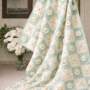 May include: A handmade crochet blanket with a floral design. The blanket features a pattern of alternating squares in cream and light blue, adorned with cream-colored 3D flowers. The blanket is draped over a decorative metal stand.
