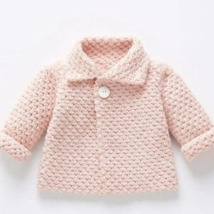 May include: A pale pink knitted baby cardigan with a collared neckline and long sleeves. It features a single, round, white button. The cuffs and collar are folded over. The knit has a textured appearance.
