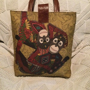 Peut inclure: Un sac cabas jaune avec une poignée en cuir marron et une illustration colorée de deux singes sur le devant.