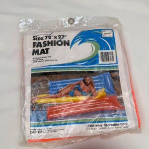 May include: A clear plastic package containing a 72 inch by 27 inch Fashion Mat. The packaging features a blue wave graphic, text reading Size 72 inch x 27 inch FASHION MAT, and a photo of a person on a blue and yellow inflatable pool float.