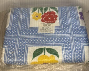 Op de afbeelding: Een nieuwe, verpakte deken met een blauw en wit stippenpatroon en bloemmotieven. De deken heeft gele, rode en paarse bloemen. Het label luidt "Butterfly & Flower Boxes" en meet 203 x 229 cm.