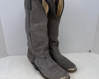 May include: A pair of grey leather cowboy boots featuring a tall shaft with decorative stitching, pull tabs at the top, and metallic silver-toned toe caps. The boots have a pointed toe design and a stacked heel, showcasing a textured finish.