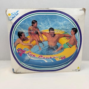 Puede incluir: Una caja de cartón cuadrada para una piscina inflable Intex The Wet Set Fun Center. La caja presenta un gráfico de un gran anillo inflable amarillo y azul con patrones florales, que mide 203 cm, con personas en su interior.