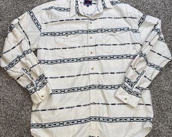 May include: Cream-colored button-down shirt with a geometric black and teal pattern. The long-sleeved shirt has two chest pockets and a button-down collar. The shirt is laid flat on a gray surface.