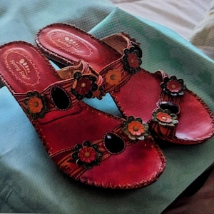 May include: A pair of red leather sandals with floral embellishments and black accents. The sandals have a brand label that reads "Spring Step".