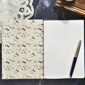 May include: A closed journal with a floral patterned cover and a blank page open to reveal a silver pen.