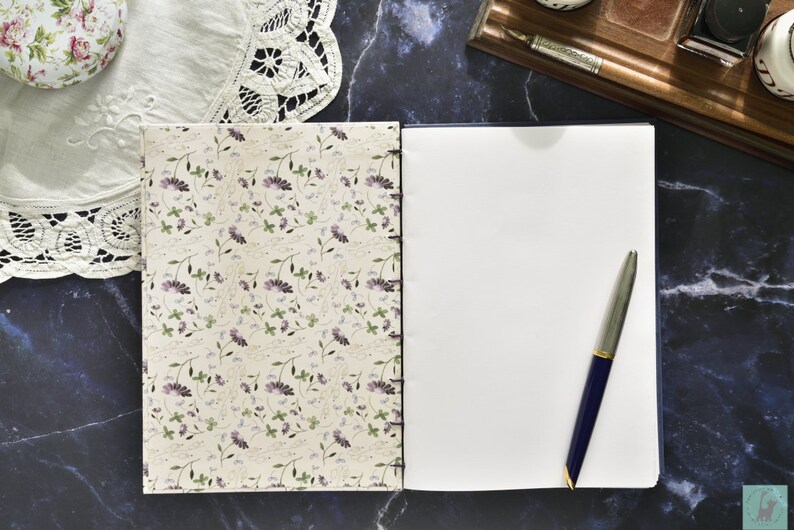 May include: A closed journal with a floral patterned cover and a blank page open to reveal a silver pen.