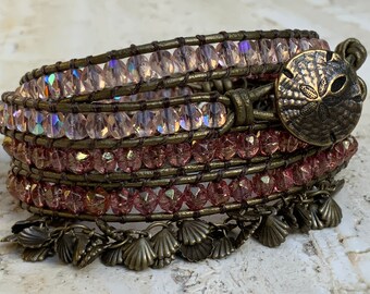May include: A multi-strand leather wrap bracelet with pink and iridescent glass beads, a sand dollar charm, and multiple shell charms.