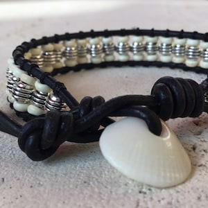 May include: A black leather bracelet with white and silver beads and a white shell charm.