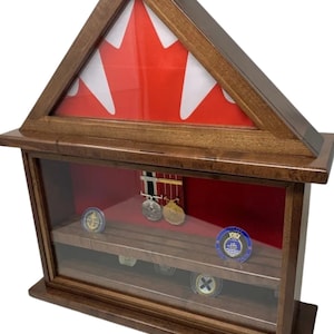 May include: A wooden shadow box with a glass front and a red felt interior. The box features a triangular top with a Canadian flag design. The box has two shelves for displaying medals and coins.