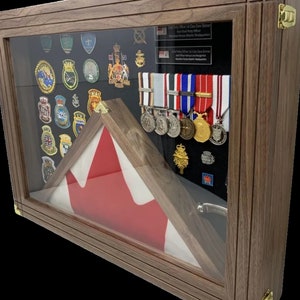 Può includere: Una teca in legno con una bandiera canadese, medaglie e toppe. Il testo sulla targa recita "Chief Petty Officer 1st Class Dave Skinner, Chief Petty Officer, Maritime Forces Atlantic Headquarters".