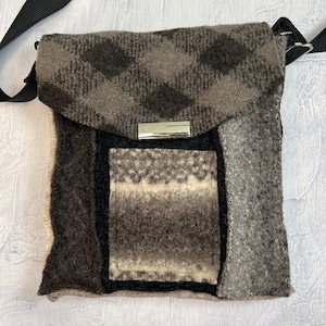 Op de afbeelding: Een klein grijs en zwart patchwork schoudertasje met een zilveren metalen sluiting. De tas heeft een klep sluiting en een klein vakje aan de voorkant.