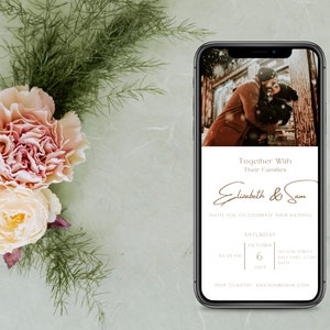 May include: A smartphone displays a wedding invitation with a photo of a couple embracing. The invitation text reads "Together With Their Families" and "Elizabeth & Sam". Soft pink and cream flowers and greenery are arranged on a light green background.