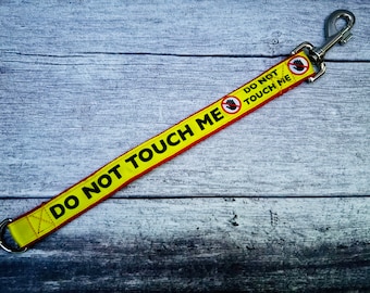 May include: A yellow and red lead with the text "DO NOT TOUCH ME" and a hand with a diagonal line through it. The lead has a silver clip.