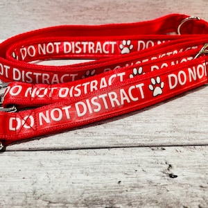 May include: Two red dog leashes with white paw prints and the text "DO NOT DISTRACT" printed on them. The leashes are made of a durable nylon material and have a metal clip.