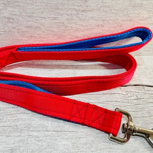 A handmade two-tone dog lead in red with marine blue padded handle and traffic handle, made from cushioned webbing with a metal trigger hook