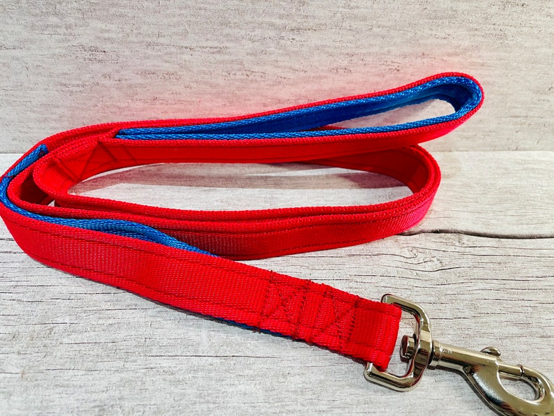 A handmade two-tone dog lead in red with marine blue padded handle and traffic handle, made from cushioned webbing with a metal trigger hook