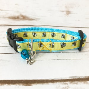May include: A yellow and blue cat collar with a bee pattern and a silver bee charm and a blue bell.