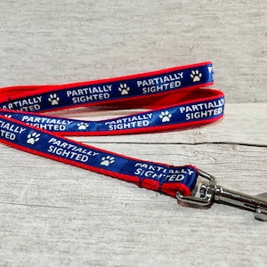 May include: Red and blue dog leash with a silver clip. The leash has the words "Partially Sighted" printed on it with a paw print.
