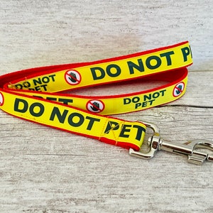 May include: A yellow and red dog leash with the text "DO NOT PET" printed on it. The leash has a silver clip.