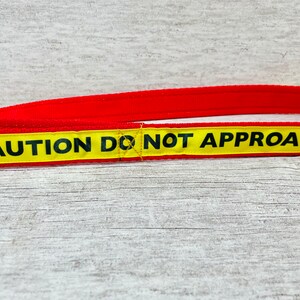May include: A red and yellow dog leash with the text "CAUTION DO NOT APPROACH" printed on it.