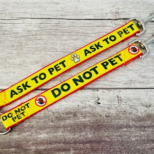 May include: Two yellow and red dog leads with metal clips. One lead says "Ask to Pet" with a paw print and the other says "Do Not Pet" with a hand with a line through it.