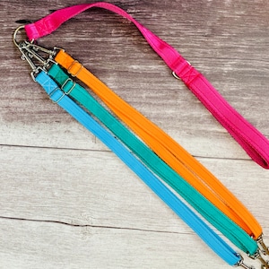 May include: A set of three dog leads in blue, teal, and orange, attached to a pink lead with a silver clip. The leads are laid out on a wooden surface.