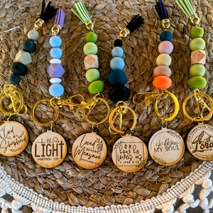 May include: Six wooden keychain charms with different religious quotes and colorful beaded tassels. The charms feature phrases like "The Lord is my Shepherd", "Little Light", "Loved Beyond Measure", "Oh how he loves us", "He restores my soul", and "My Help Comes from the Lord".