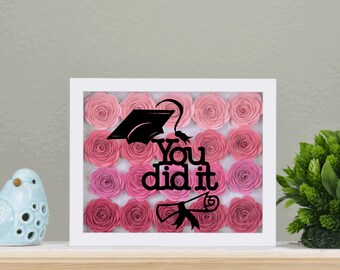May include: White frame with a pink and white paper flower background. The text "You did it" is in black with a graduation cap and diploma.