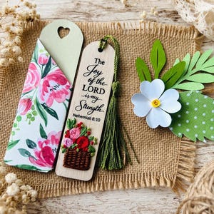 May include: A wooden bookmark with the text "The Joy of the LORD is my Strength" and a floral basket design. A matching floral patterned gift envelope and a paper flower with green leaves are also present. The items are arranged on a burlap surface.