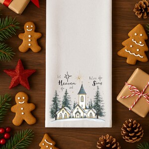 May include: A white Christmas-themed kitchen towel with a church and pine tree illustration. The text "Let Heaven and Nature Sing" is printed on the towel. The image is surrounded by gingerbread cookies, a red star, and wrapped gifts.