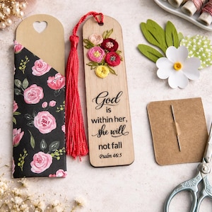 May include: Wooden bookmark with embroidered flowers and a red tassel. The bookmark has the text "God is within her, she will not fall Psalm 46:5". A floral patterned bookmark holder is also present.
