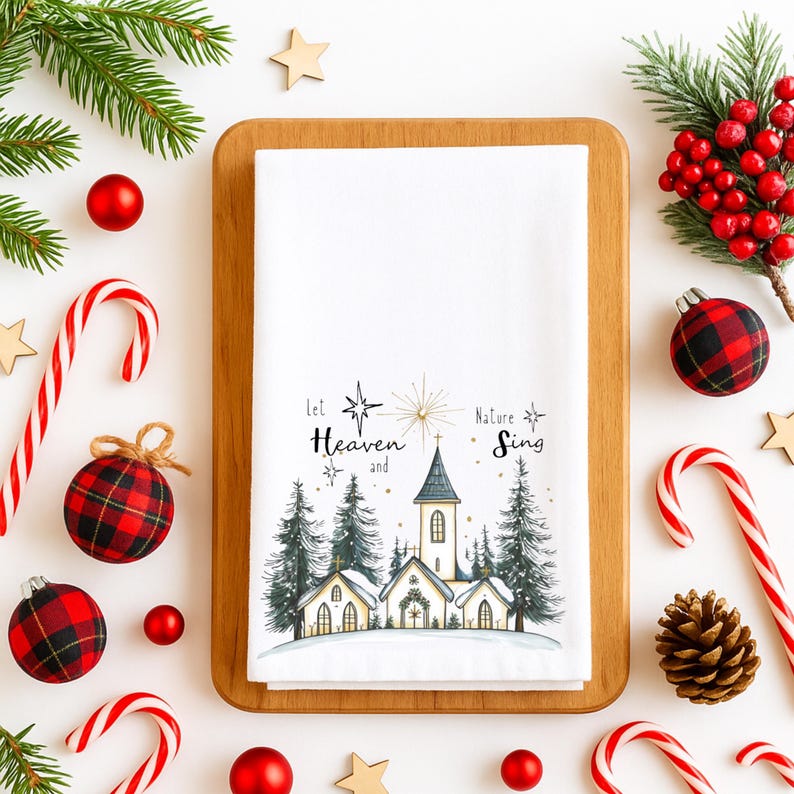 May include: White Christmas-themed kitchen towel with a church and pine tree illustration. The text "Let Heaven and Nature Sing" is printed on the towel. The towel is surrounded by Christmas decorations, including candy canes, ornaments, and greenery.