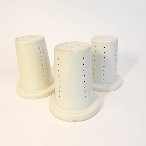 May include: Three white ceramic funnels with small holes throughout the sides. The funnels are all the same size and shape.